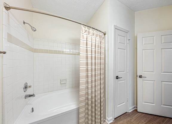 A white bathroom with a shower, tub, and two doors.