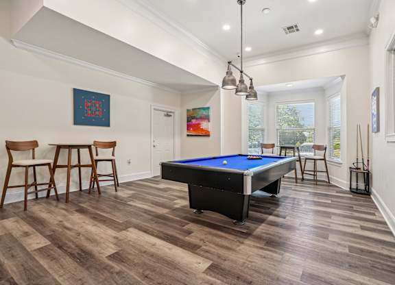 A pool table is in the middle of a room with wood flooring.
