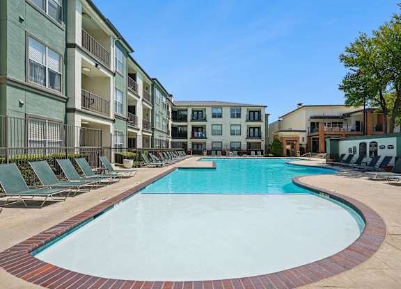 A swimming pool surrounded by lounge chairs in front of apartment buildings.