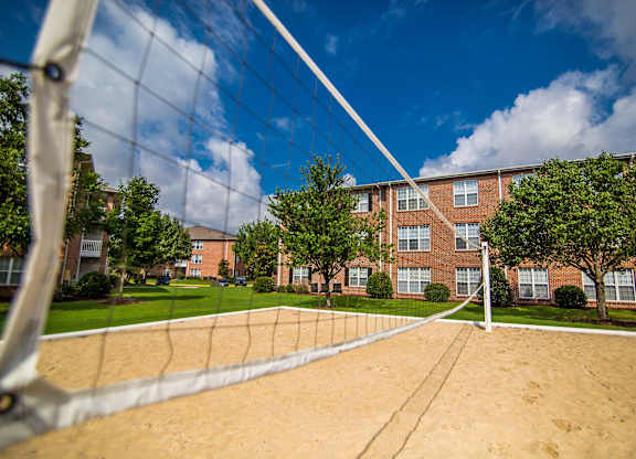 A volleyball net is in the foreground of a sandy court with apartment buildings in the background.