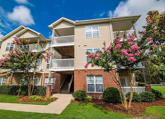 A large apartment building with a front lawn and flowering trees.