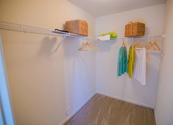 A white closet with clothes hanging and baskets on the shelf.