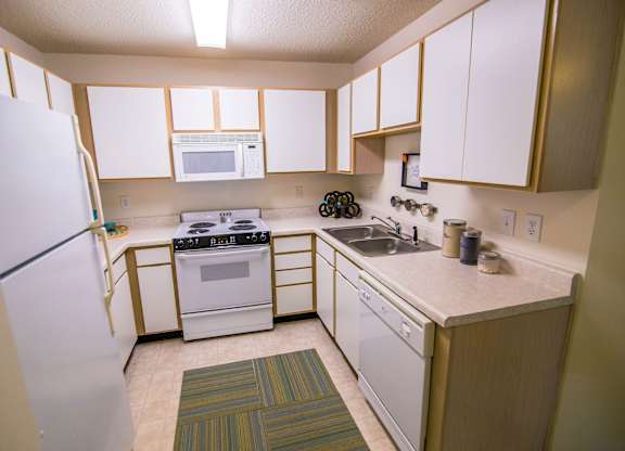 A kitchen with white appliances and a green rug.