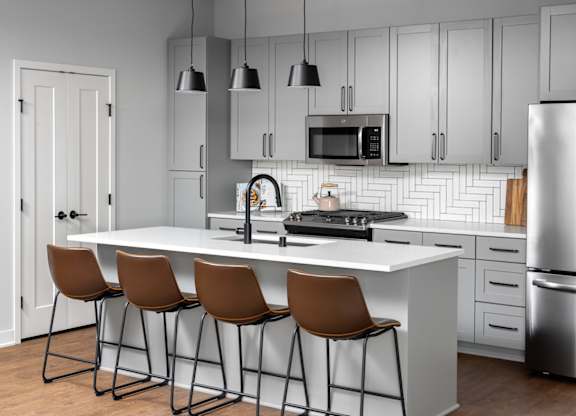 A modern kitchen with a white island and brown barstools.