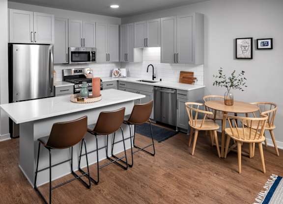 A modern kitchen with a white island and wooden chairs.