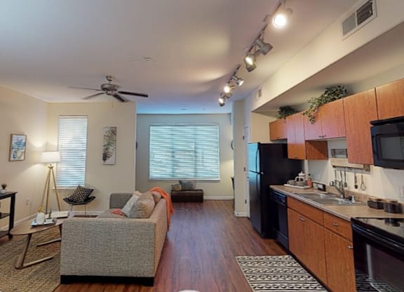 A living room with a couch, a television, and a kitchen area with a refrigerator, microwave, and oven.
