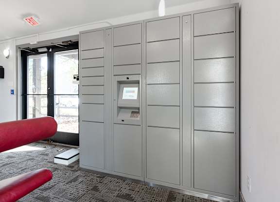 A grey metal locker room with a red bench and a door with a window.
