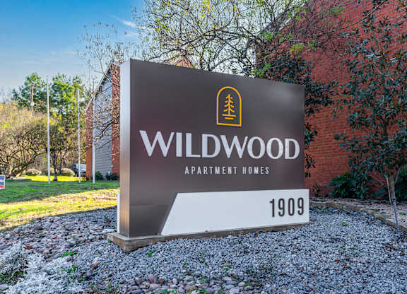 A sign for Wildwood Apartment Homes is displayed in front of a brick building.