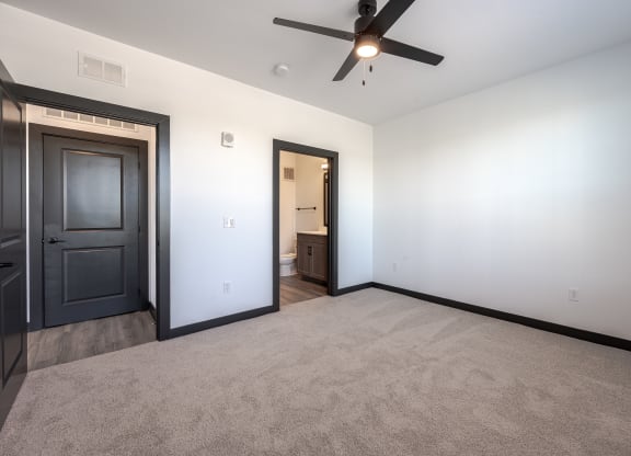 an empty living room with a ceiling fan and a door to a bathroom