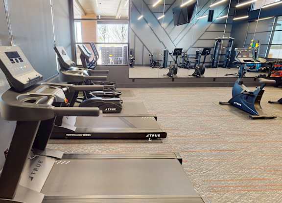 A treadmill with a digital display is in a gym with other exercise equipment.