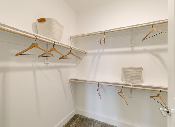 a walk in closet with white walls and wooden hangers