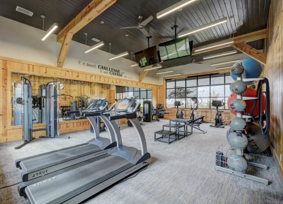 Spacious gym here at 35 Degrees North Apartment Homes with wooden walls, treadmills, weight racks, exercise balls, and rowing machines. Bright lighting and large windows create an energetic atmosphere.
