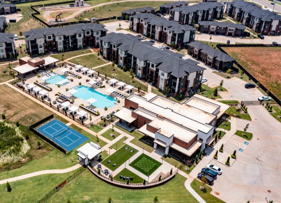 Aerial view of 35 Degrees North Apartment Homes complex with modern buildings, a large central pool surrounded by loungers, and a tennis court, set in a landscaped area.