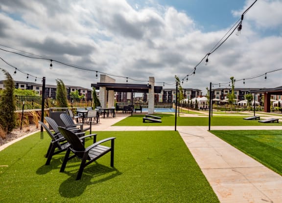 Outdoor patio here at 35 Degrees North Apartment Homes with artificial grass, Adirondack chairs, string lights, and a modern fire pit. Overcast sky adds a calm, inviting atmosphere.