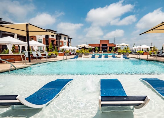 Luxurious outdoor pool here at 35 Degrees North Apartment Homes with cascading water features, blue lounge chairs, and large umbrellas. Modern apartments and cabanas frame the vibrant scene.