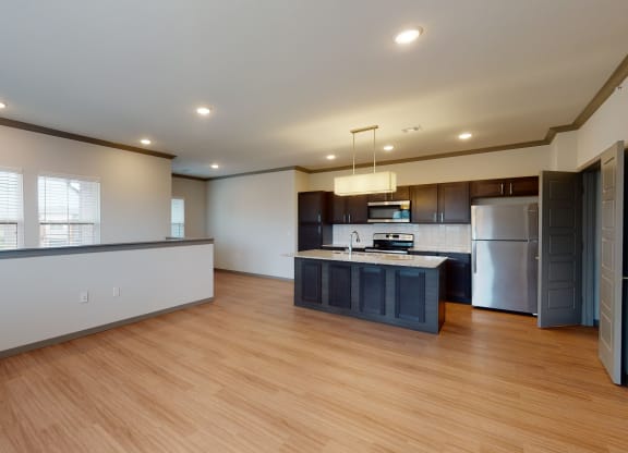 Modern kitchen here at 35 Degrees North Apartment Homes with stainless steel appliances, dark wood cabinets, and a granite island. Open floor plan with bamboo flooring and recessed lighting.