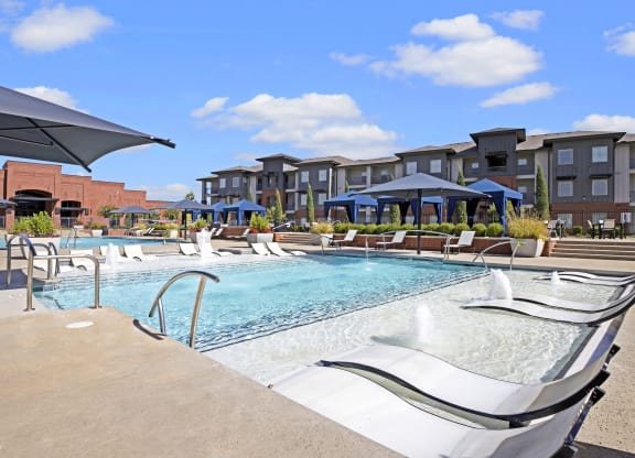 a swimming pool with chairs and umbrellas in front of an apartment building