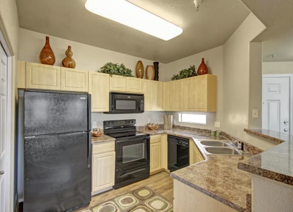 Modern kitchen here at Natura Villas Apartments with light wood cabinets, black appliances, and marble countertops. Decorative vases and greenery adorn the upper cabinets for a cozy touch.