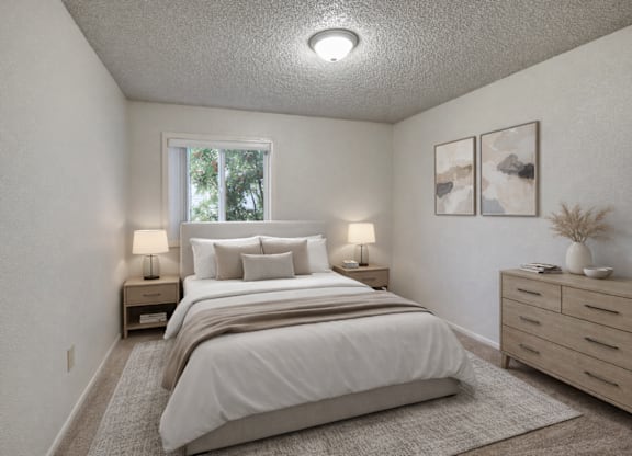 A cozy bedroom at Arctic Sun Apartments with a queen bed dressed in soft white bedding and neutral pillows. Two bedside tables with lamps sit on each side. A wide dresser with décor and wall art adds style, and a window lets in natural light, brightening the calm, neutral space.