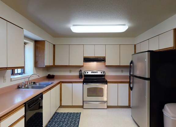 Birchwood kitchen with cream and wood cabinets, pink countertops, stainless steel appliances, and a window above the sink.