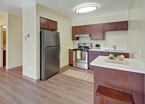 A modern kitchen here at Century Plaza featuring rich wood cabinetry, stainless-steel appliances, and a sleek breakfast bar with decorative accents. Light walls and wood-style flooring brighten the space, while ample counter areas and overhead storage create a clean, functional layout ideal for cooking and gathering.
