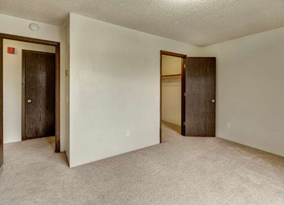 Spacious bedroom here at Deer Park showcasing soft carpet flooring, light neutral walls, and a clean, open layout. The room features a walk-in closet with shelving, a separate entry door, and ample wall space for flexible furniture placement, creating a comfortable and functional sleeping area.