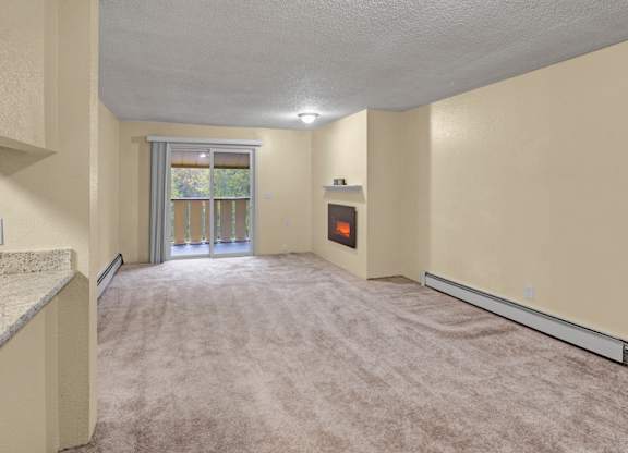 An open living room space here at Hillside Chalet with a carpeted floor and a sliding door window with a view of trees. A cozy fireplace sits against the wall next to the sliding doors.
