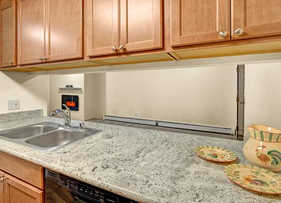 A kitchen with a granite countertop, a stainless steel sink, and wooden cabinets.