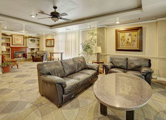 A spacious community lounge here at Mendenhall-Tower with leather sofas, a round granite table, and a warm fireplace framed by built-in shelving.