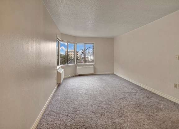A bright, open living space here at Mendenhall-Tower with soft gray carpeting, neutral walls, and large corner windows that bring in beautiful natural light and scenic views.