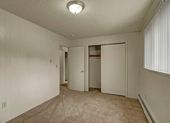 A spacious, empty bedroom here at Montclair with beige carpet, light paneled walls, and a sliding-door closet for convenient storage.