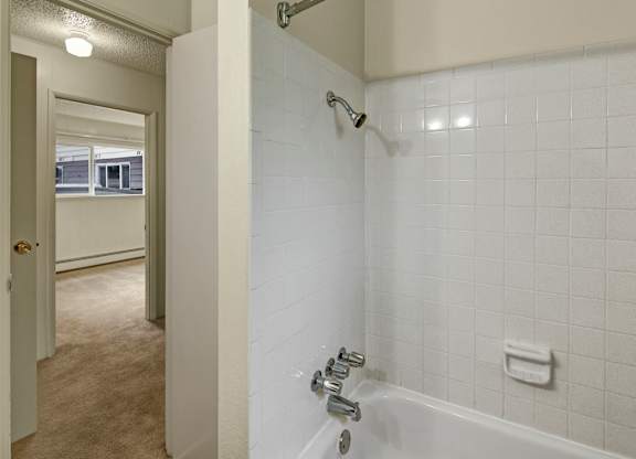 A clean bathtub-shower combo here at Montclair with white tiled walls, chrome fixtures, and a built-in soap holder for simple convenience.