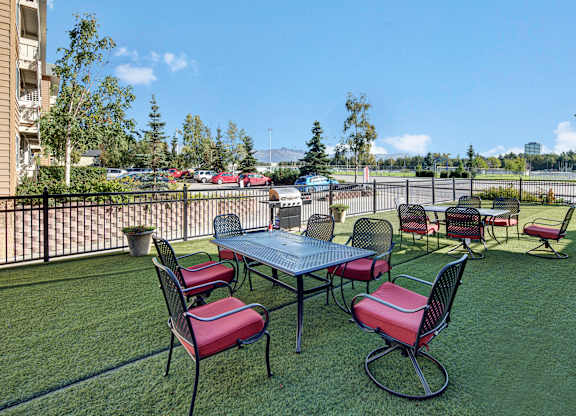 A sunny outdoor patio area here at Park Plaza II, with metal tables and chairs featuring red cushions, offering open views of the surrounding neighborhood and a relaxed space for outdoor seating.