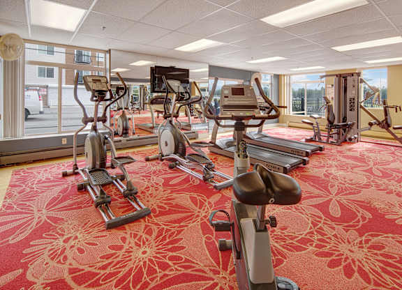 A bright fitness center here at Park Plaza II with cardio and strength equipment including treadmills, ellipticals, and weight machines, featuring large windows and mirrors for an open, energetic workout space.