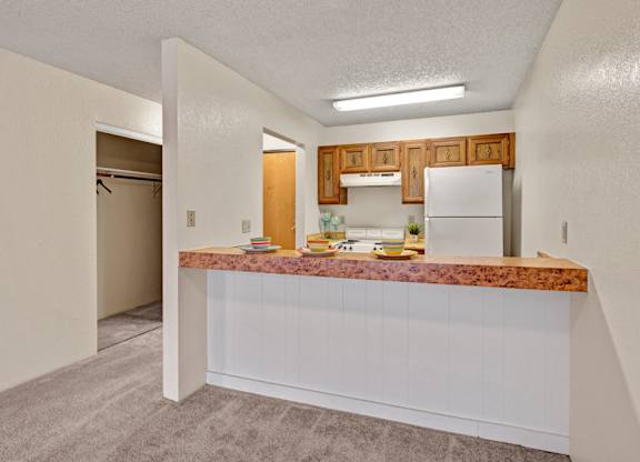 A cozy kitchen here at Park Plaza with a wide breakfast bar and marbled countertop, featuring warm wood cabinets, a white stove and refrigerator, and bright overhead lighting for a clean, functional feel.