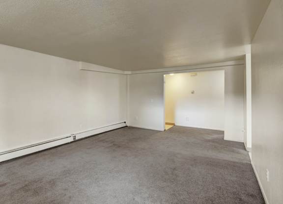 A spacious, empty living room here at Ptarmigan Meadows with soft gray carpet, clean white walls, and an open layout that offers plenty of room for flexible furniture placement.