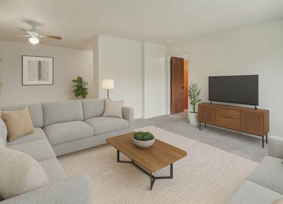 A bright living room here at Rancho Tudor with a light gray sectional sofa, a wooden coffee table, a soft neutral rug, and a modern TV console with simple greenery accents.