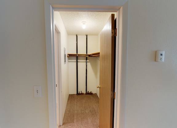 A long closet area here at Rancho Tudor with carpeted flooring, a hanging rod for storage, and a simple layout for organizing everyday essentials.