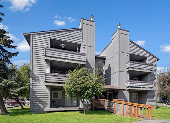 A grey building with a balcony and a tree in front.