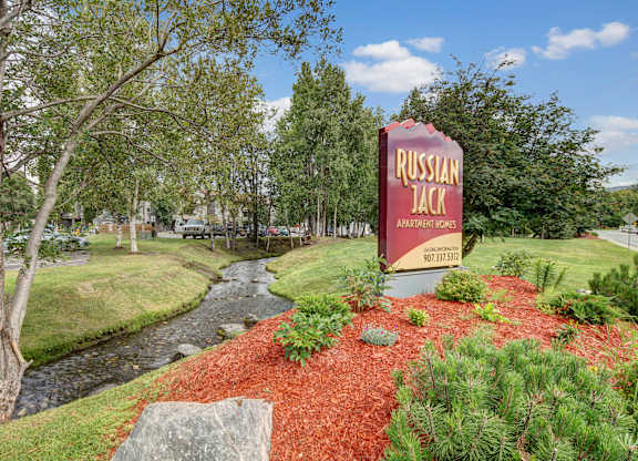 A sign for Russian Jack Apartments stands in front of a stream.