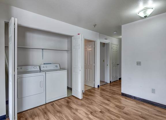 A convenient in-home laundry area here at Silver Ridge with a full-size washer and dryer tucked into a dedicated closet space. A wood-style hallway floor and nearby storage shelf create a clean, functional setup with easy access to the rest of the home.