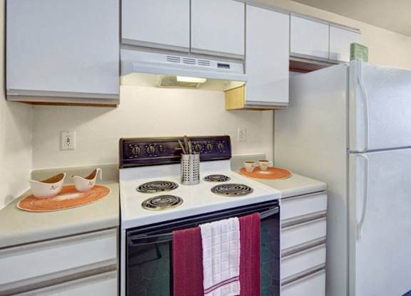A clean kitchen here at Timber Ridge with white cabinets, white countertops, and a white refrigerator, featuring an stove with range hood and a simple, bright layout for everyday cooking.