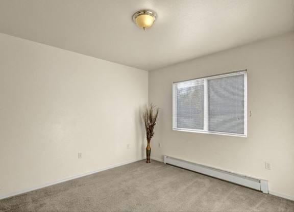 A bright, empty bedroom here at Timber Ridge with soft beige carpet, clean white walls, and a wide window with blinds that brings in natural light for a calm, comfortable feel.