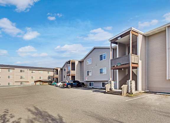A sunny exterior view here at Timber Ridge featuring multi-story apartment buildings with private balconies, ample parking, and a wide open lot under a bright blue sky for a welcoming community feel.