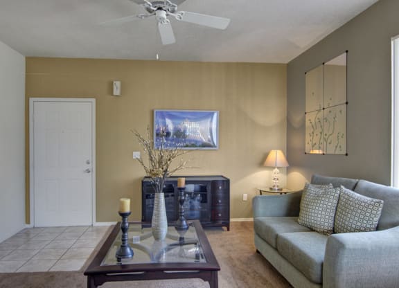 Living room here at Arezzo Apartments with a green sofa and patterned cushions, a glass and wood coffee table with candles, and a decorative wall mirror. A warm lamp glows softly.
