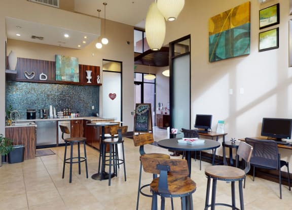 Modern lounge area here at Acclaim Apartments with wooden high tables, stools, and computers. Features a kitchenette with mosaic tiles, contemporary art, and large pendant lights.