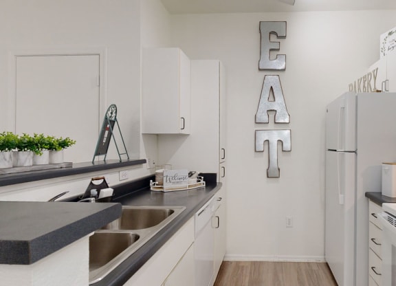 Modern kitchen here at Bolero Apartments with white cabinets, black countertops, and stainless steel appliances. Large "EAT" sign on the wall adds a welcoming touch.
