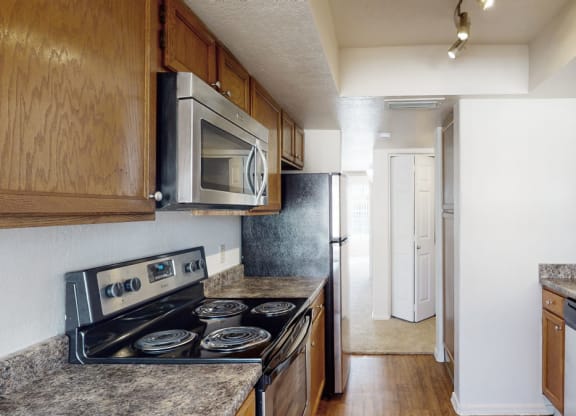 Modern kitchen here at Desert Horizon Apartments with wooden cabinets, stainless steel appliances, and granite countertops. Bright lighting creates a warm, inviting atmosphere.