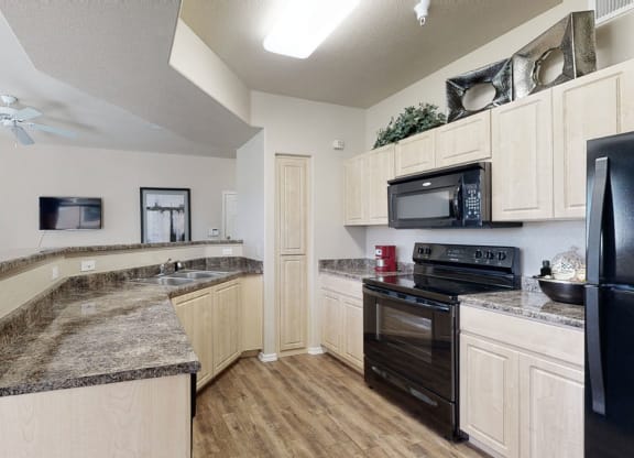 Modern kitchen here at Natura Villas Apartments with light wood cabinets, dark countertops, and black appliances including a stove and fridge. Open layout with a cozy, inviting ambiance.