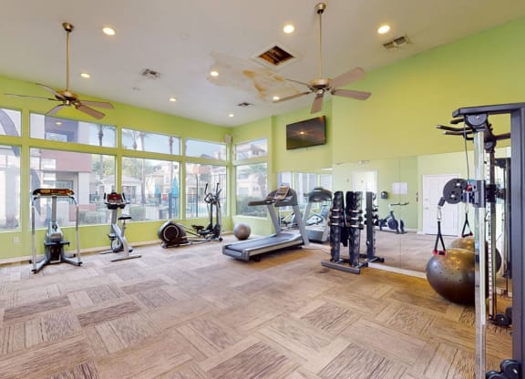 Bright gym room here at The Hawthorne Apartments with green walls and large windows, featuring treadmills, stationary bikes, and strength equipment. Mirrors enhance spaciousness.
